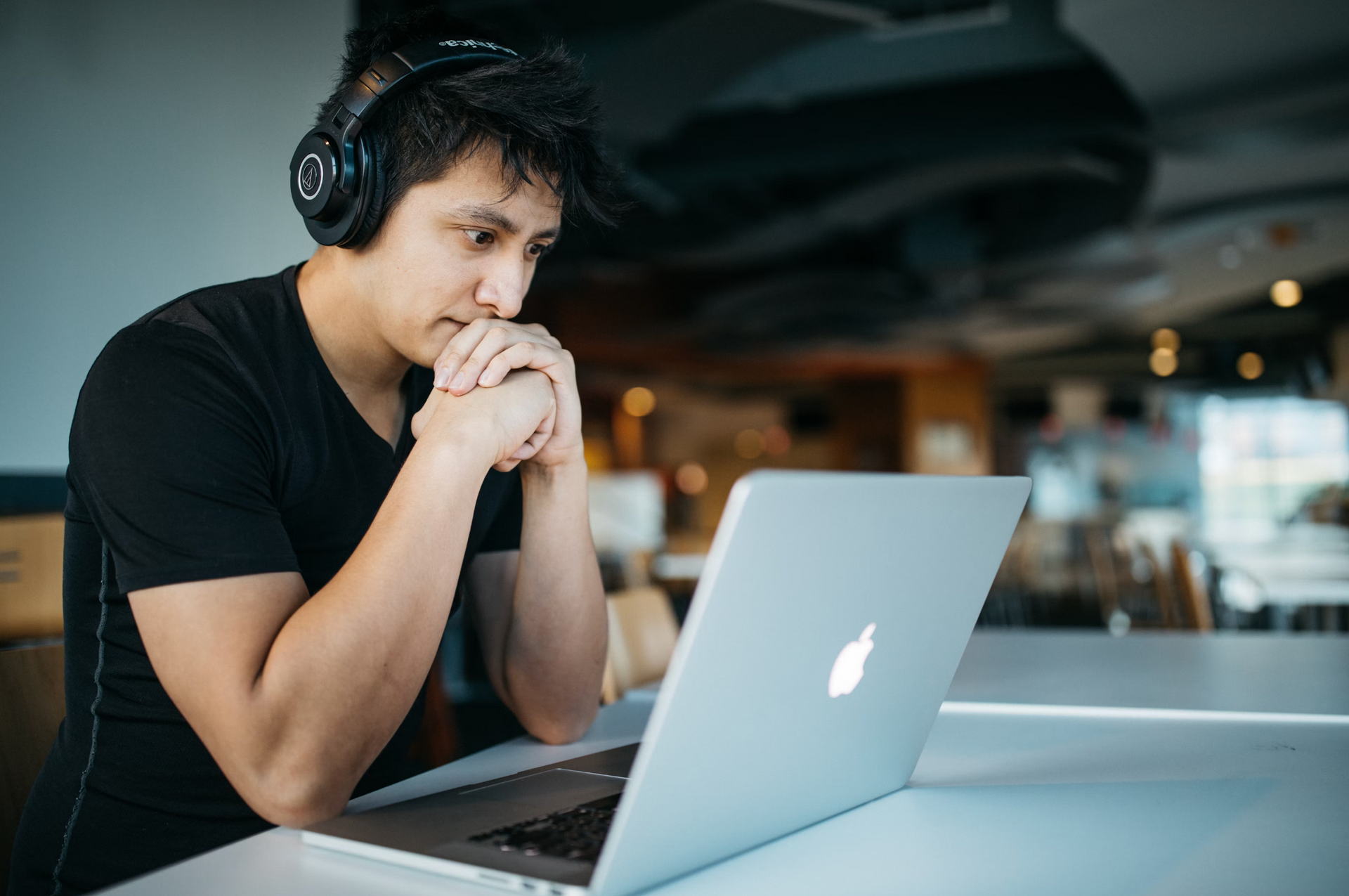 A man wearing headphones is sitting at a table looking at a laptop computer for virtual missionary training.