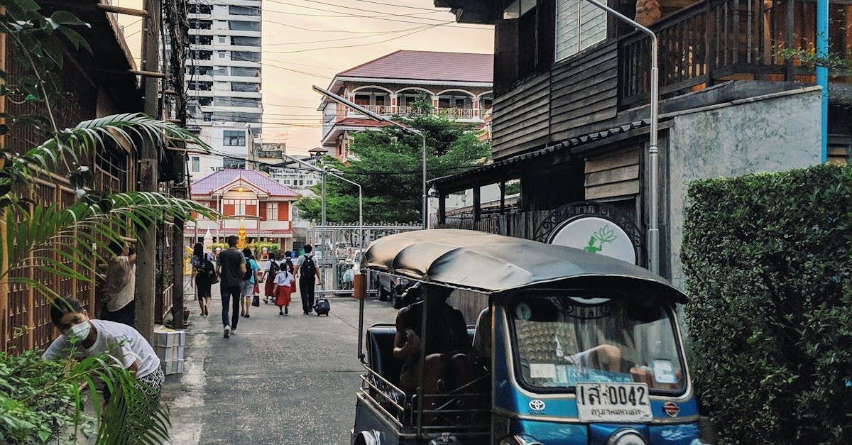Tuk-tuk parked on a city street; pedestrians walk towards colorful buildings.