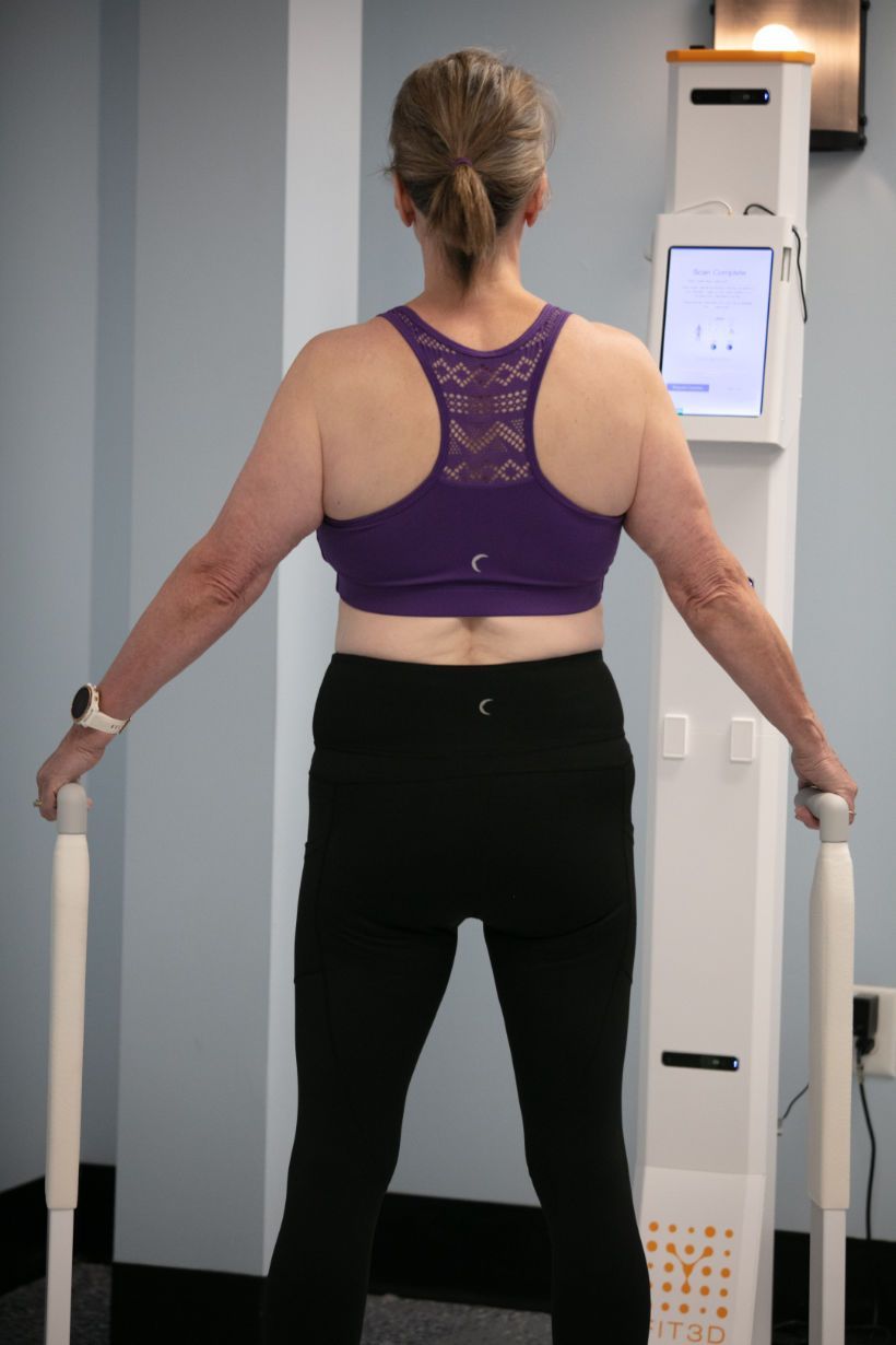 A woman in a purple top and black pants is standing in front of a machine.