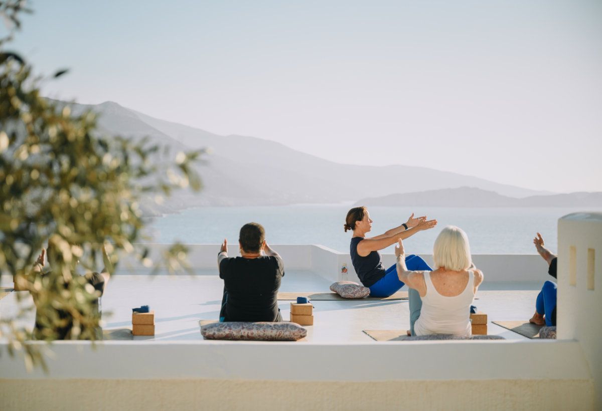 People doing yoga on a white rooftop overlooking a body of water and mountains.