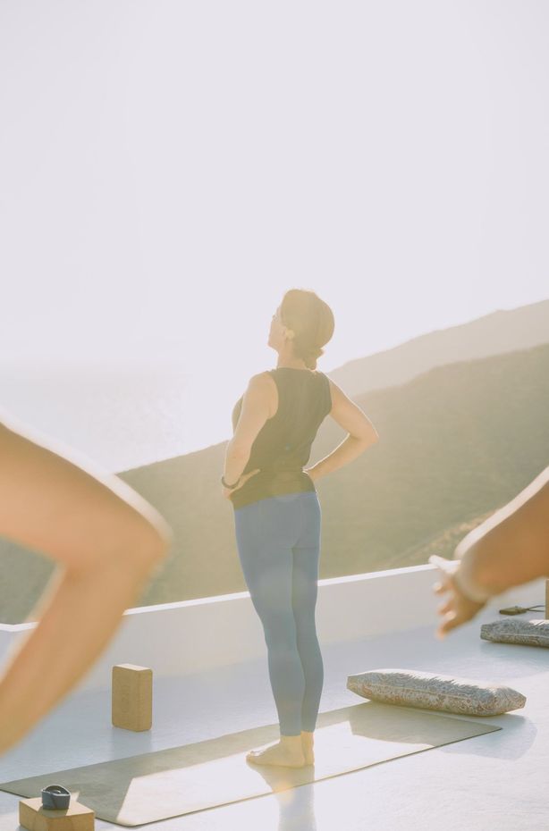 Woman in yoga pose, hands on hips, outdoors on a sunny day.