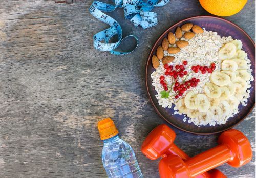 A plate of food , dumbbells , a measuring tape and a bottle of water on a wooden table.