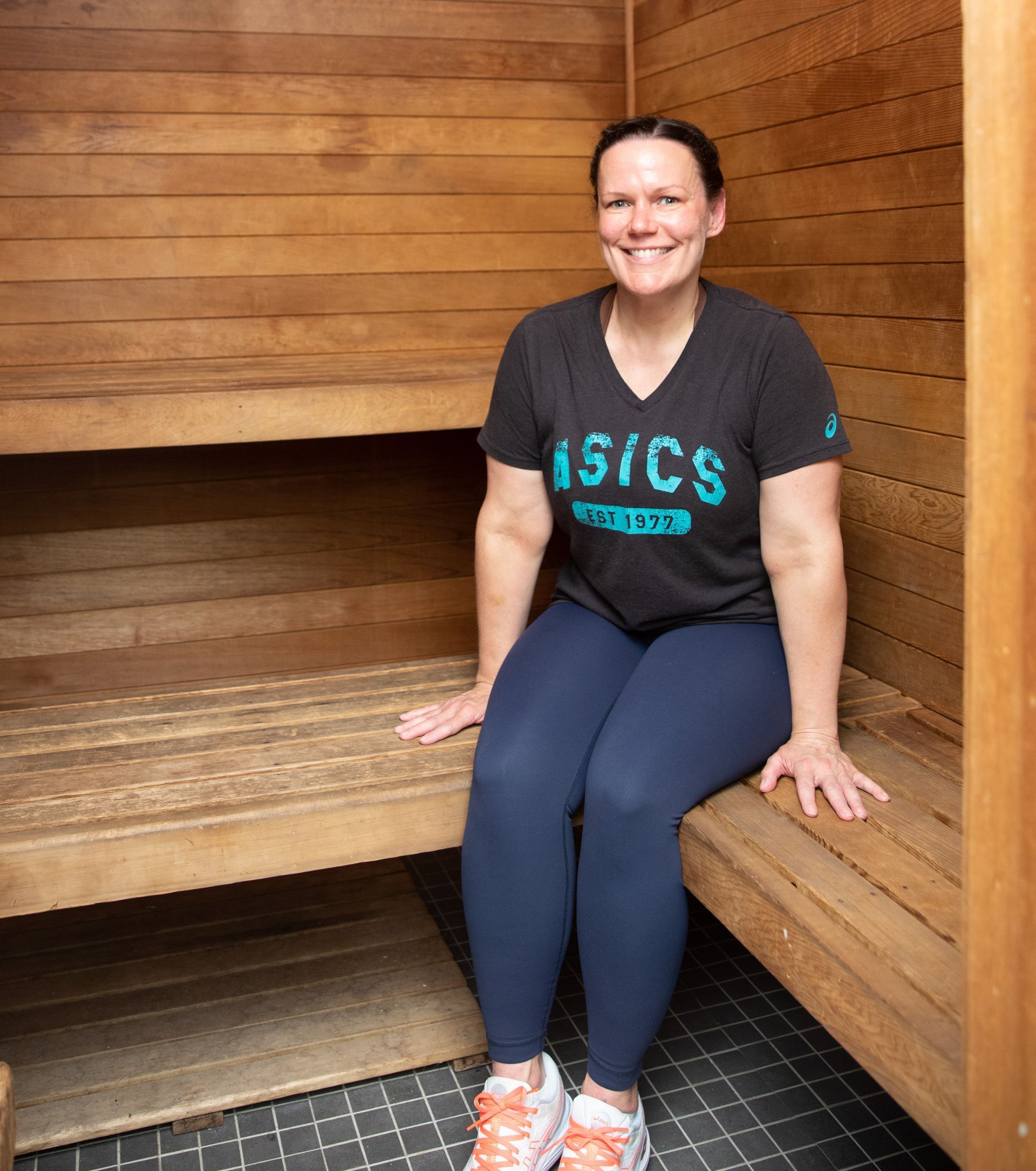 A woman wearing an asics shirt sits on a wooden bench