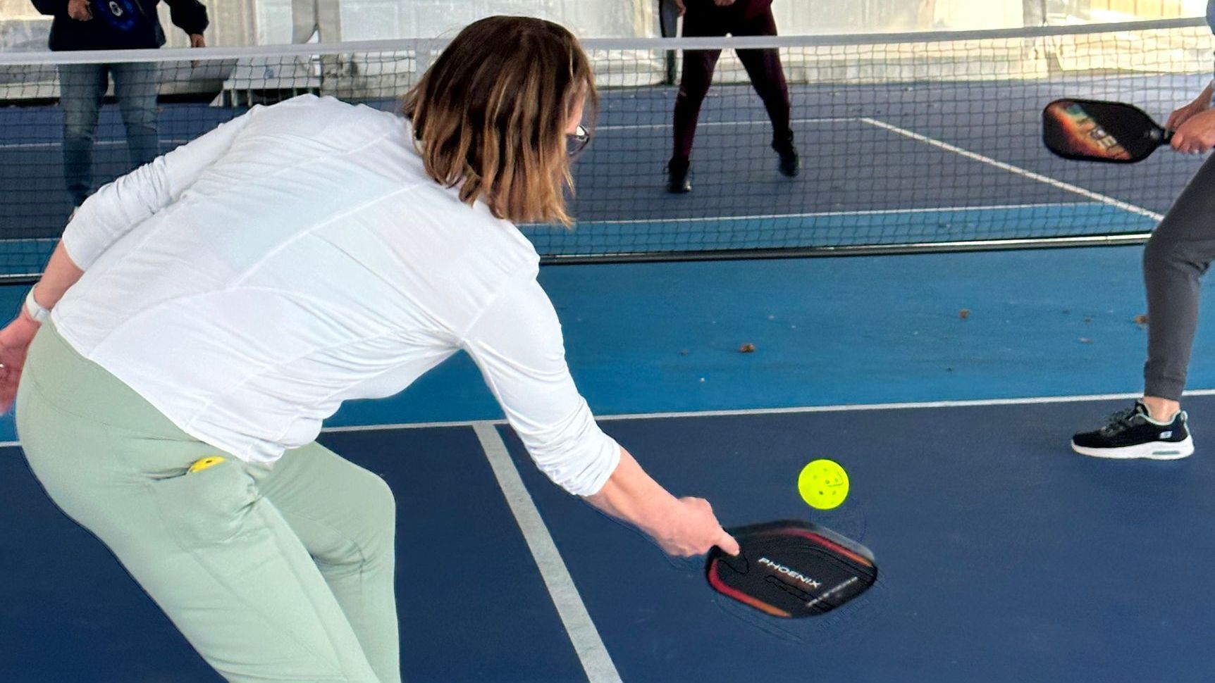 A woman is playing a game of pickleball on a tennis court.