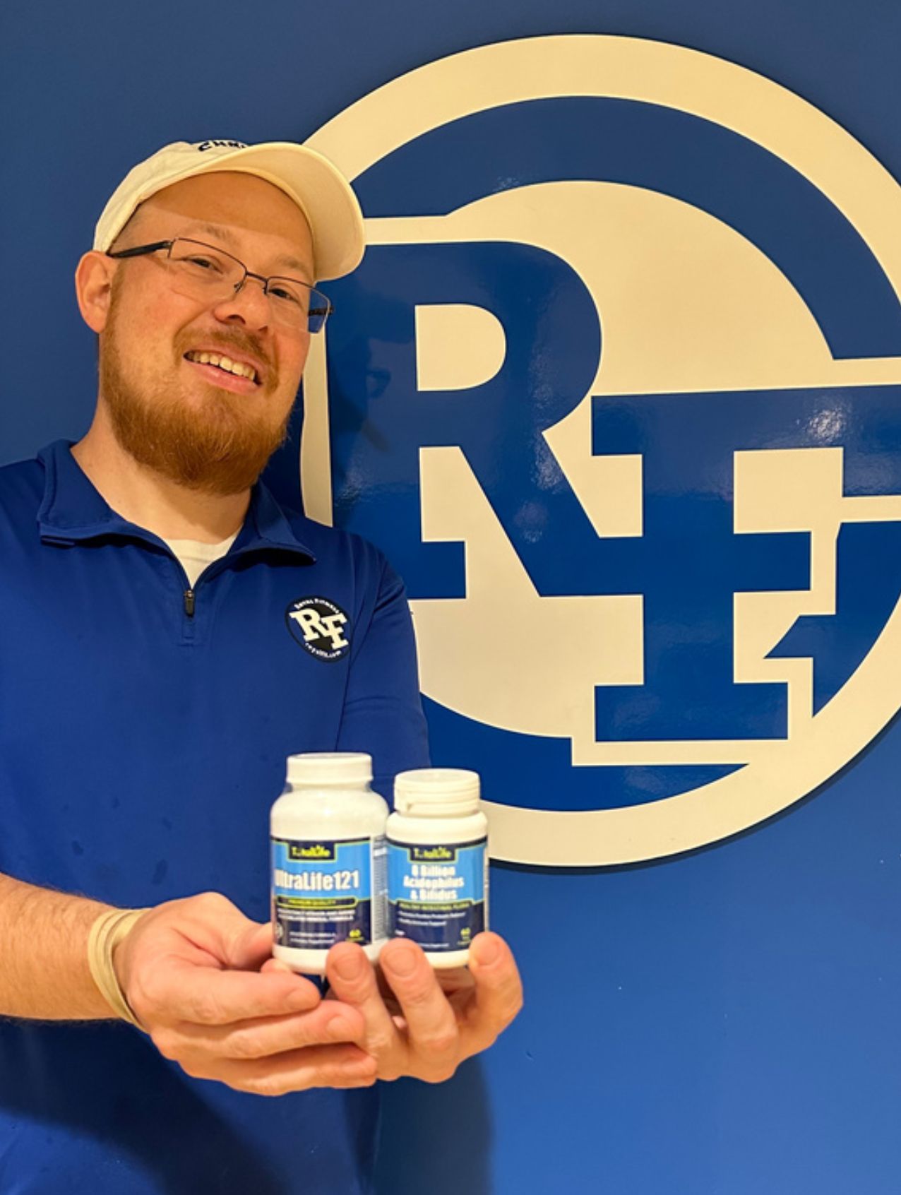 A man in a blue shirt is holding two bottles of pills in front of a r logo.