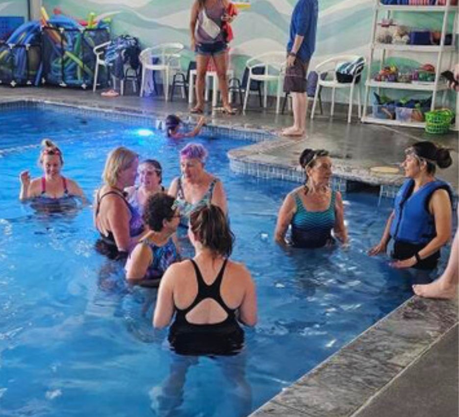 A group of women are standing in a swimming pool talking to each other.