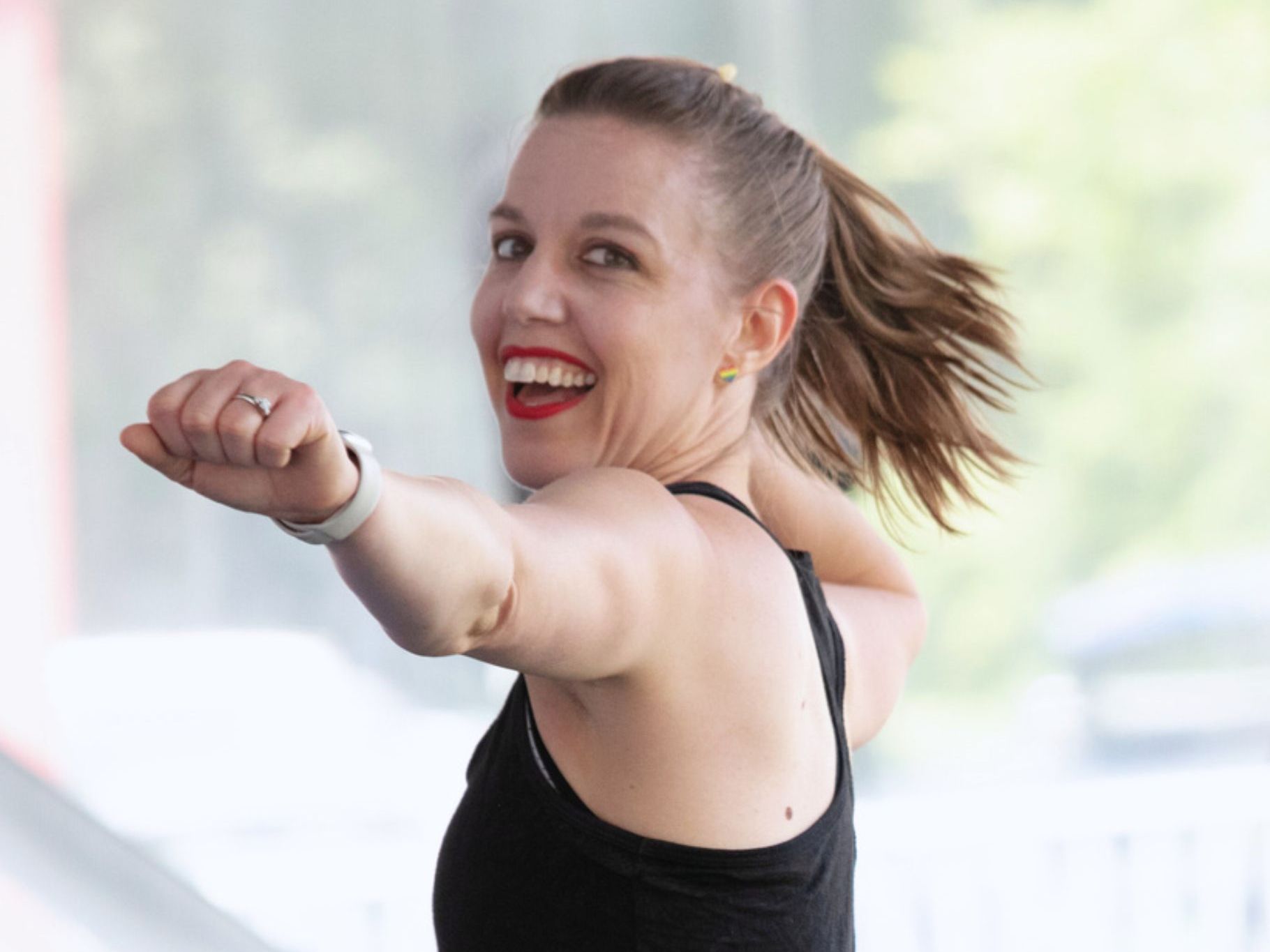 A woman in a black tank top is smiling and pointing at the camera.