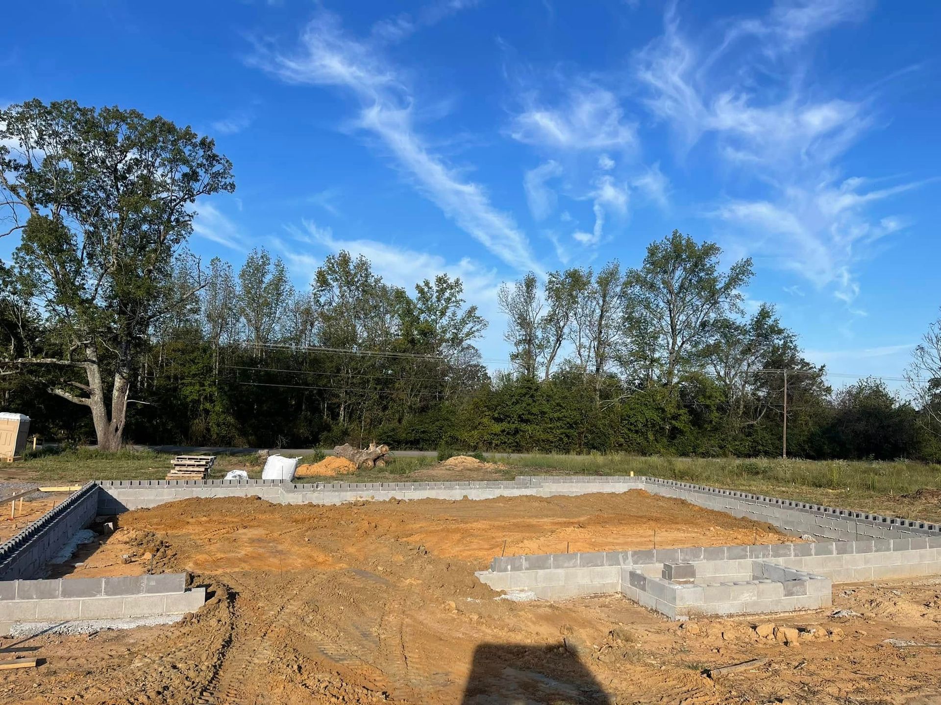 Construction site featuring a concrete block foundation for a new building on an open, grassy lot under a blue sky.
