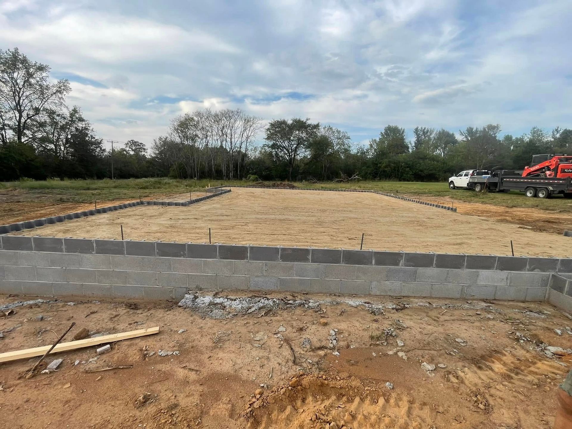A concrete block foundation for a new home under construction, with a sandy lot and trees in the background.