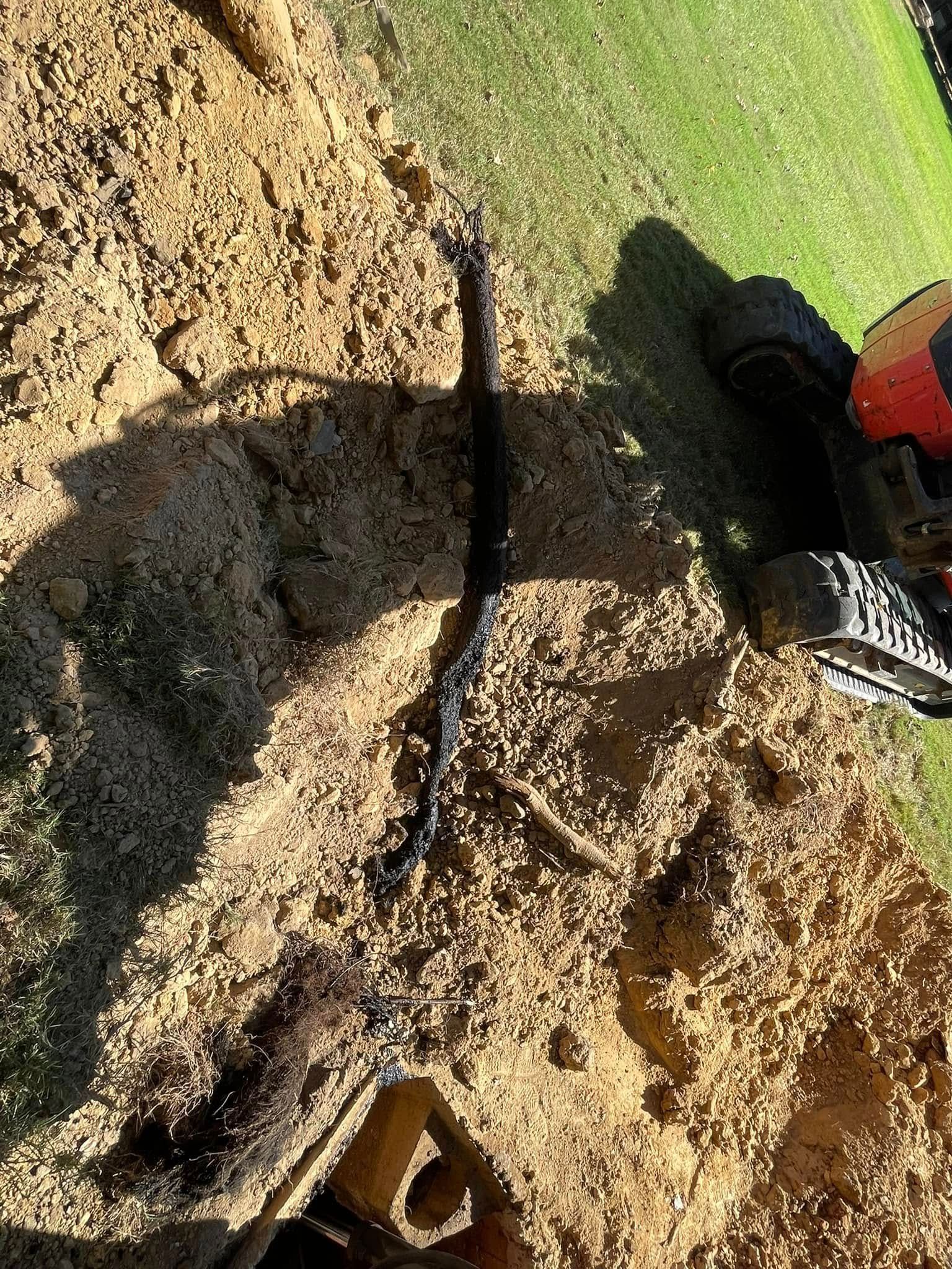 A close-up view of an exposed black utility cable lying in a dirt trench next to construction equipment.