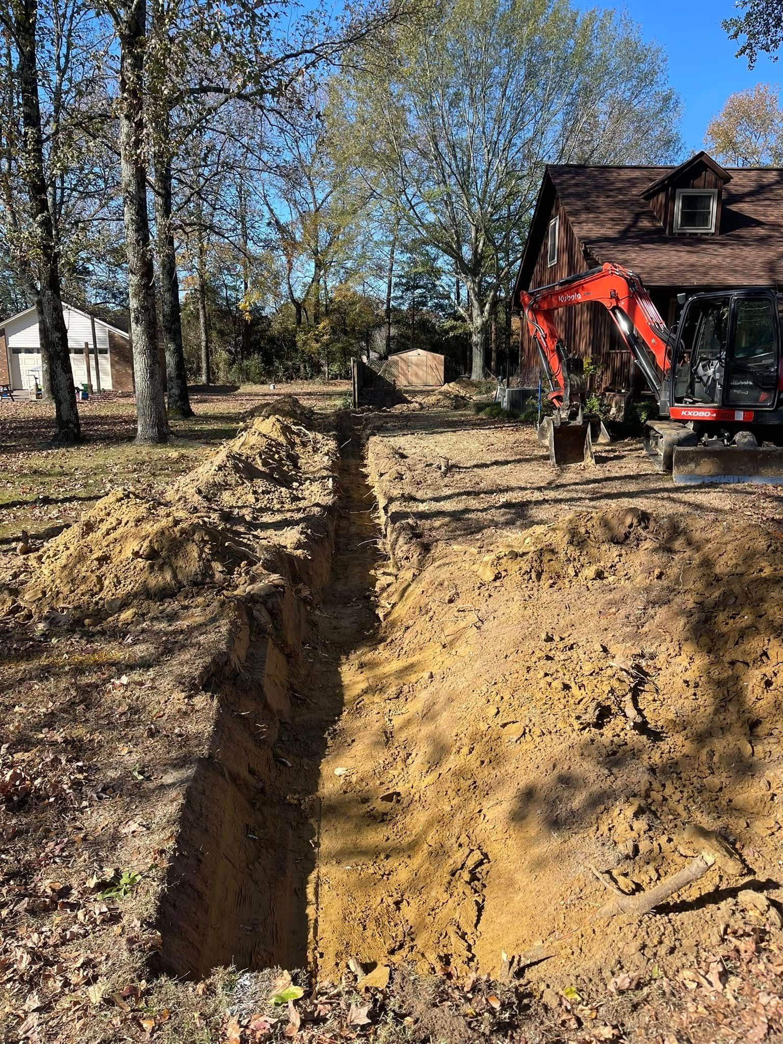 A bright red excavator sits near a long, deep trench dug into the dirt in a residential backyard on a sunny day.