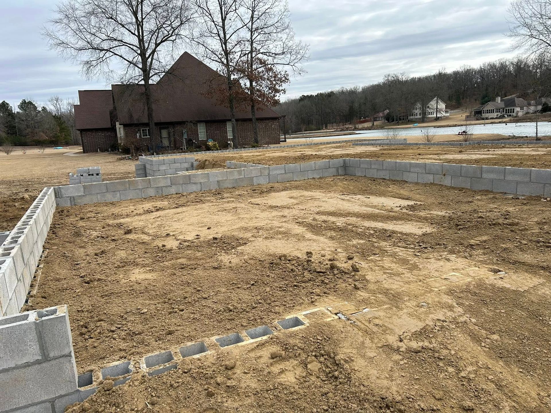 Cinder block foundation walls for a new building under construction in a grassy yard, with a house visible in the distance.