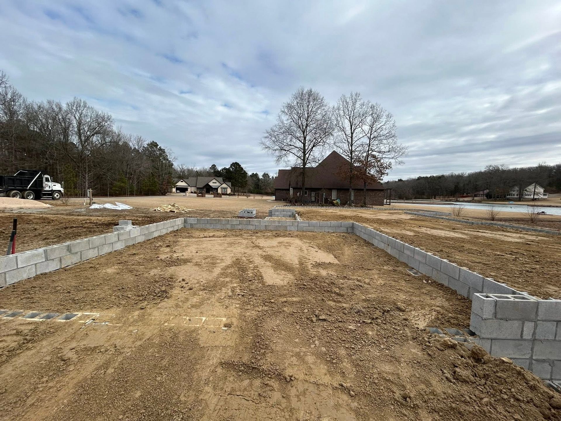 Concrete block foundation walls under construction at a rural building site with a house in the distance.