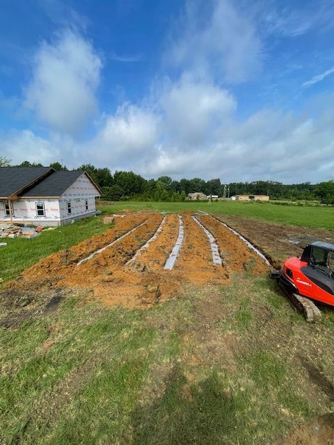 Excavated trenches for a septic field next to a house under construction on a sunny day.