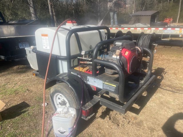 A trailer-mounted pressure washer system with a large water tank, an engine, and hose reels, parked on a grassy outdoor lot.