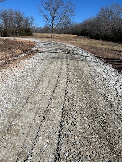 A gravel driveway leads through a rural landscape with bare trees under a clear blue sky.