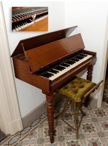 Een oude piano staat op een tegelvloer naast een kruk.