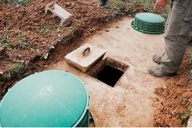 A man is standing next to a septic tank in the dirt.