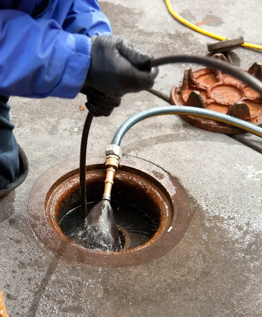 A person is working on a manhole cover with a hose