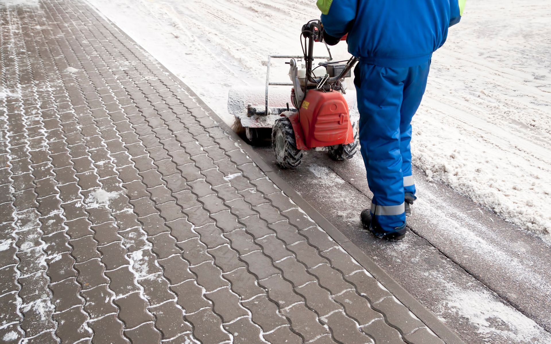 A man is using a snow blower to clean the sidewalk.