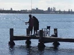 A man and a woman are fishing on a dock in the water.