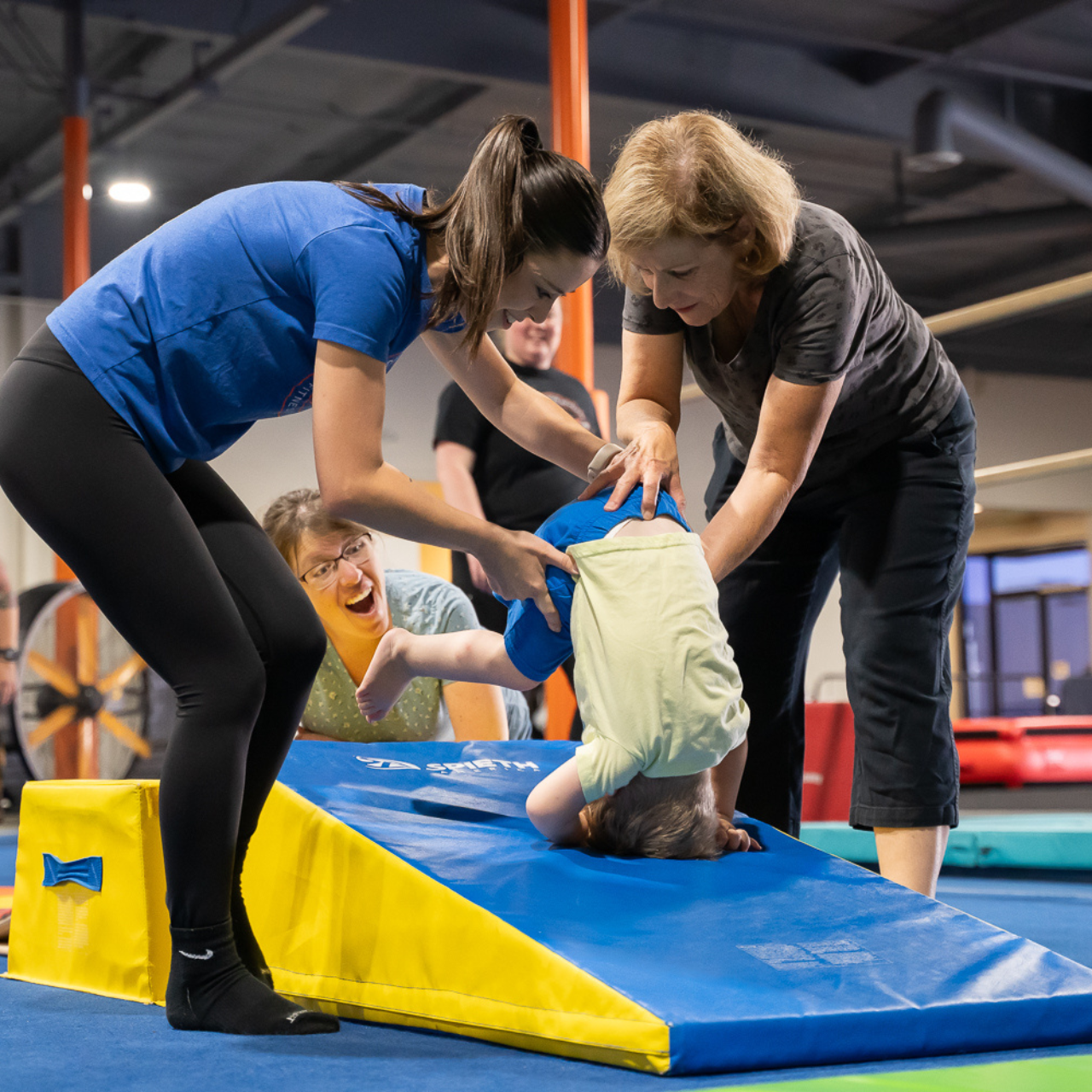 A group of people are playing with a child on a mat in a gym.