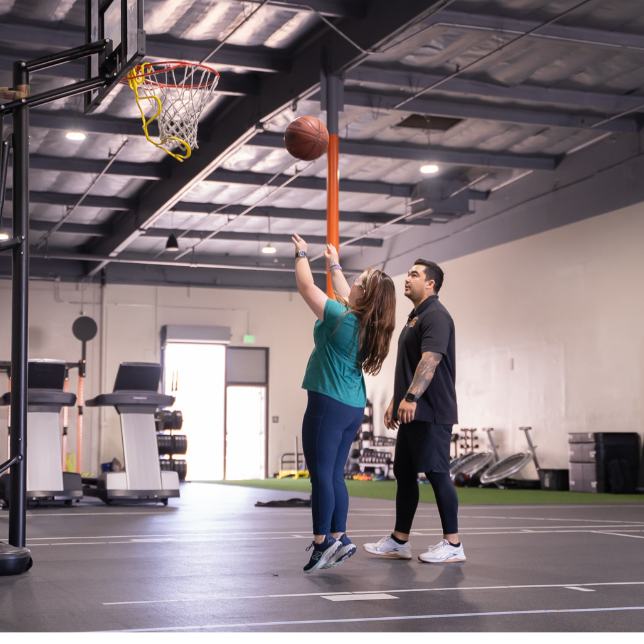 A man and a woman are playing basketball in a gym