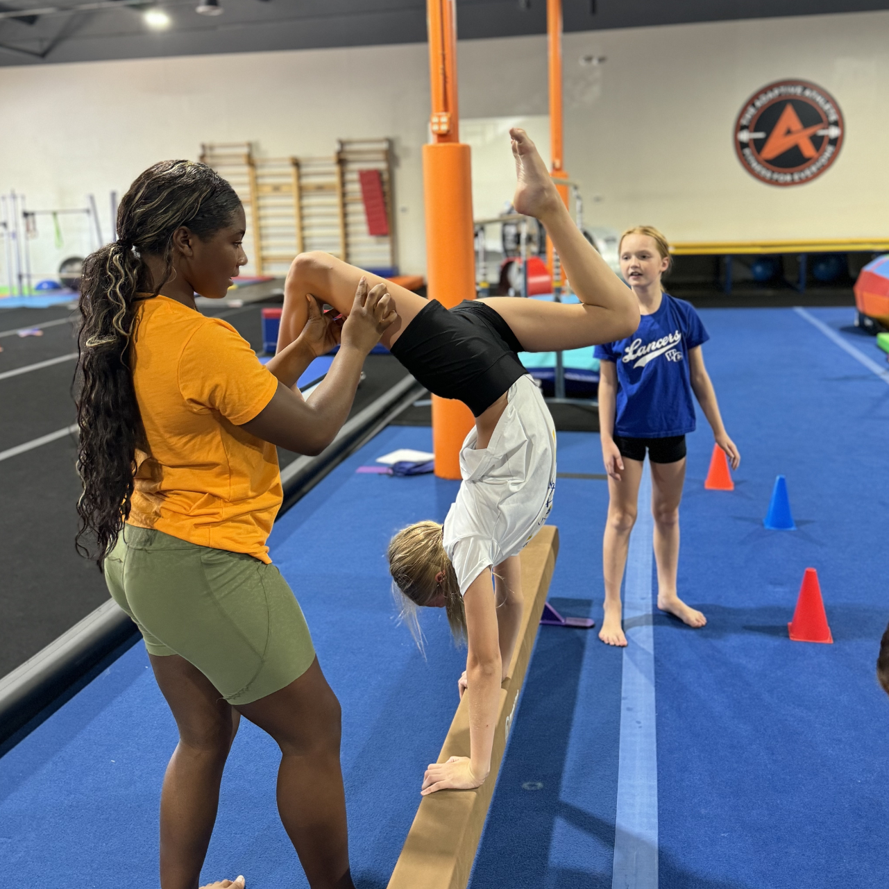 A woman is helping a  girl do a handstand on a balance beam