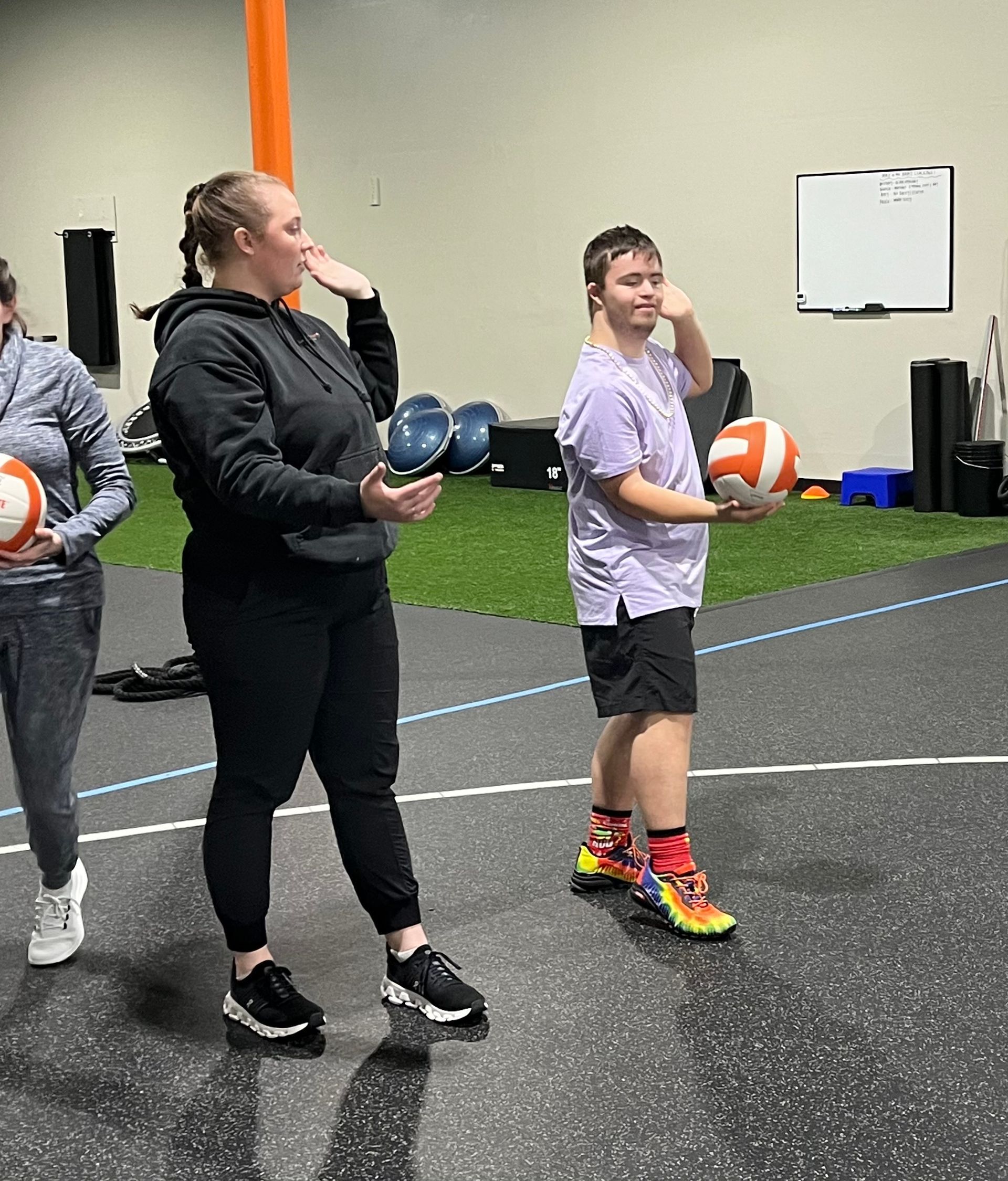 A group of people are standing in a gym holding balls and dumbbells.