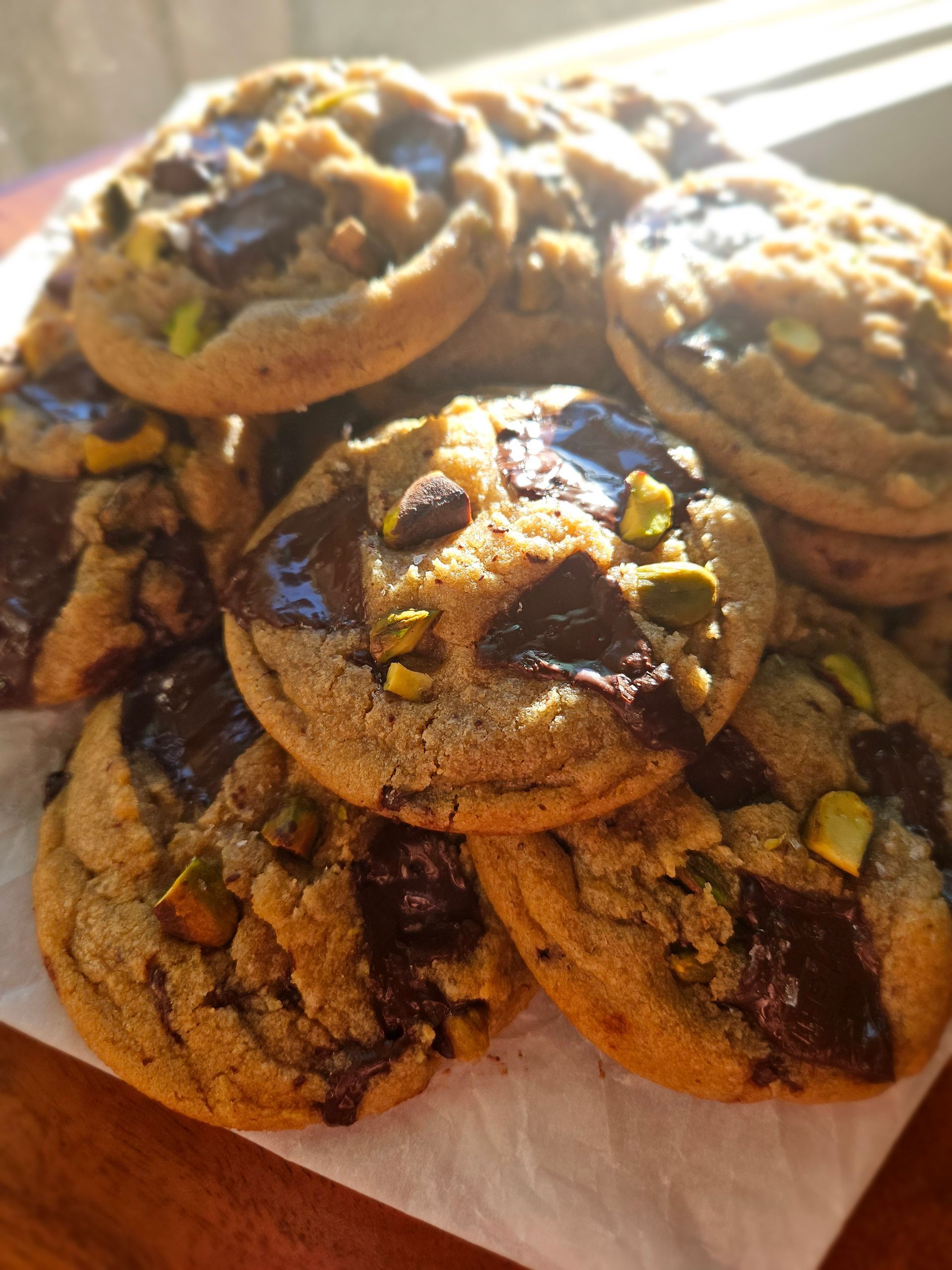 Stack of chocolate chip cookies topped with chopped pistachios on parchment paper.