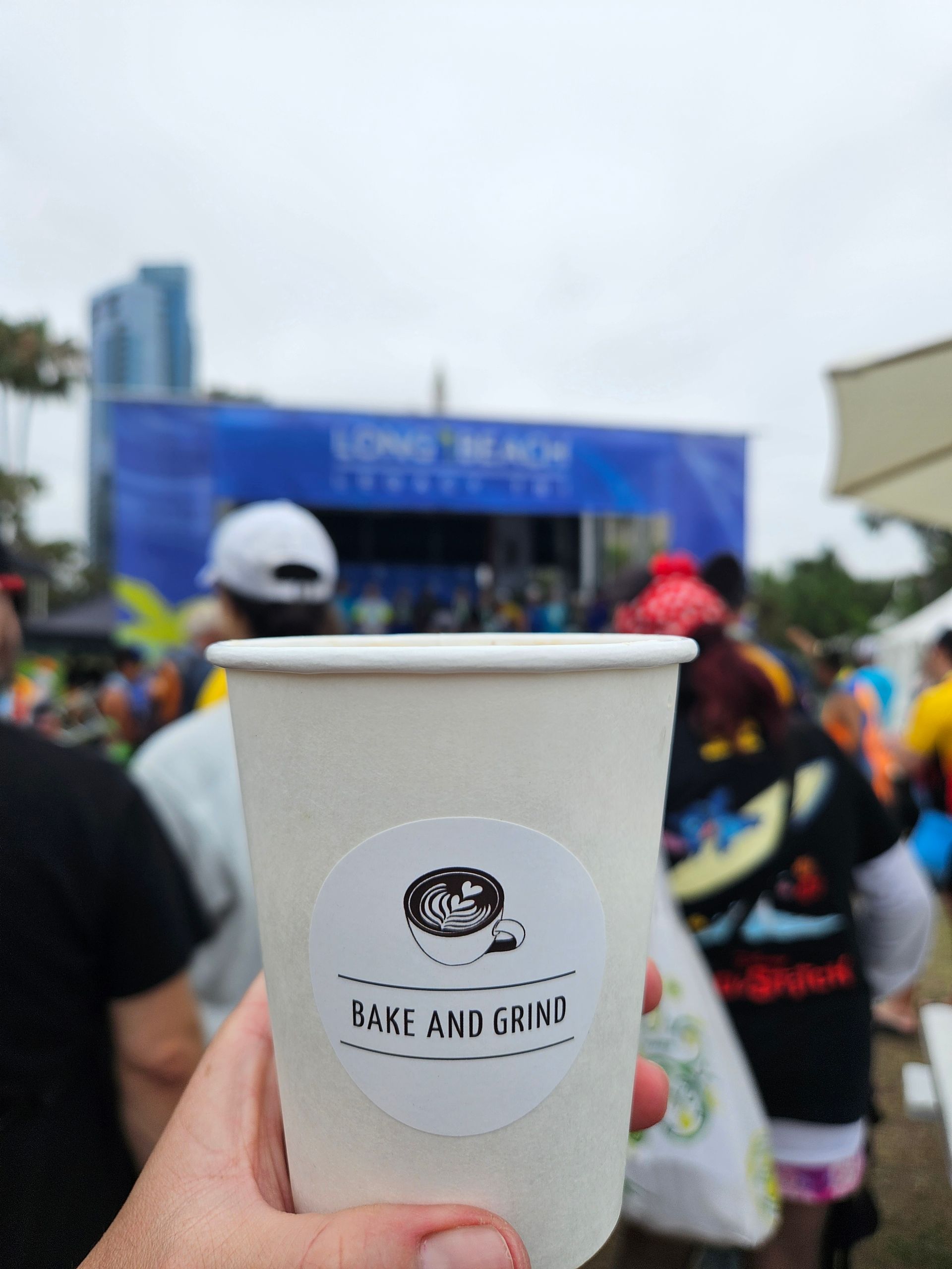 Hand holding a paper cup with a beach logo at a crowded outdoor event stage.