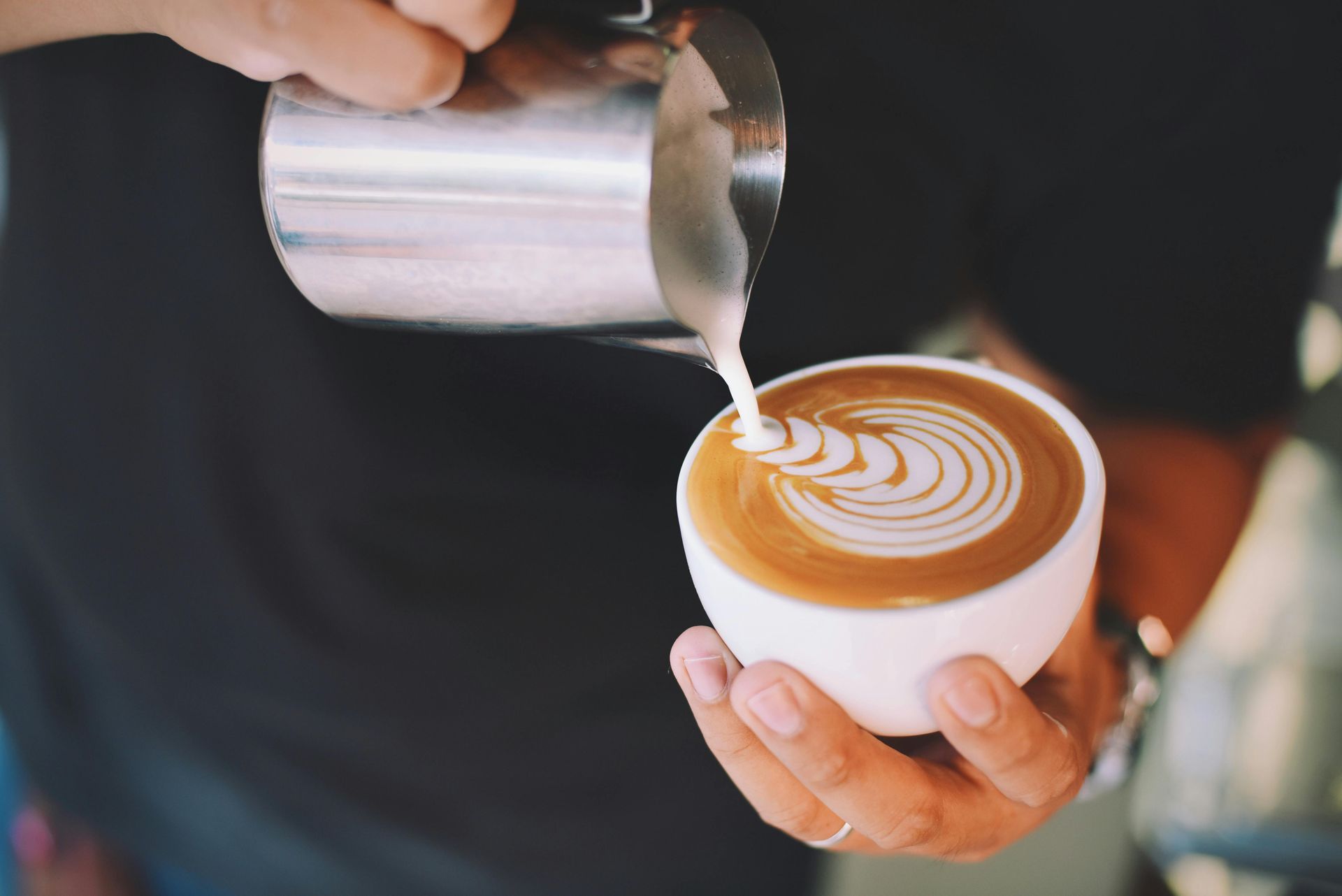 Barista pours milk into a latte, creating a heart latte art in a white cup