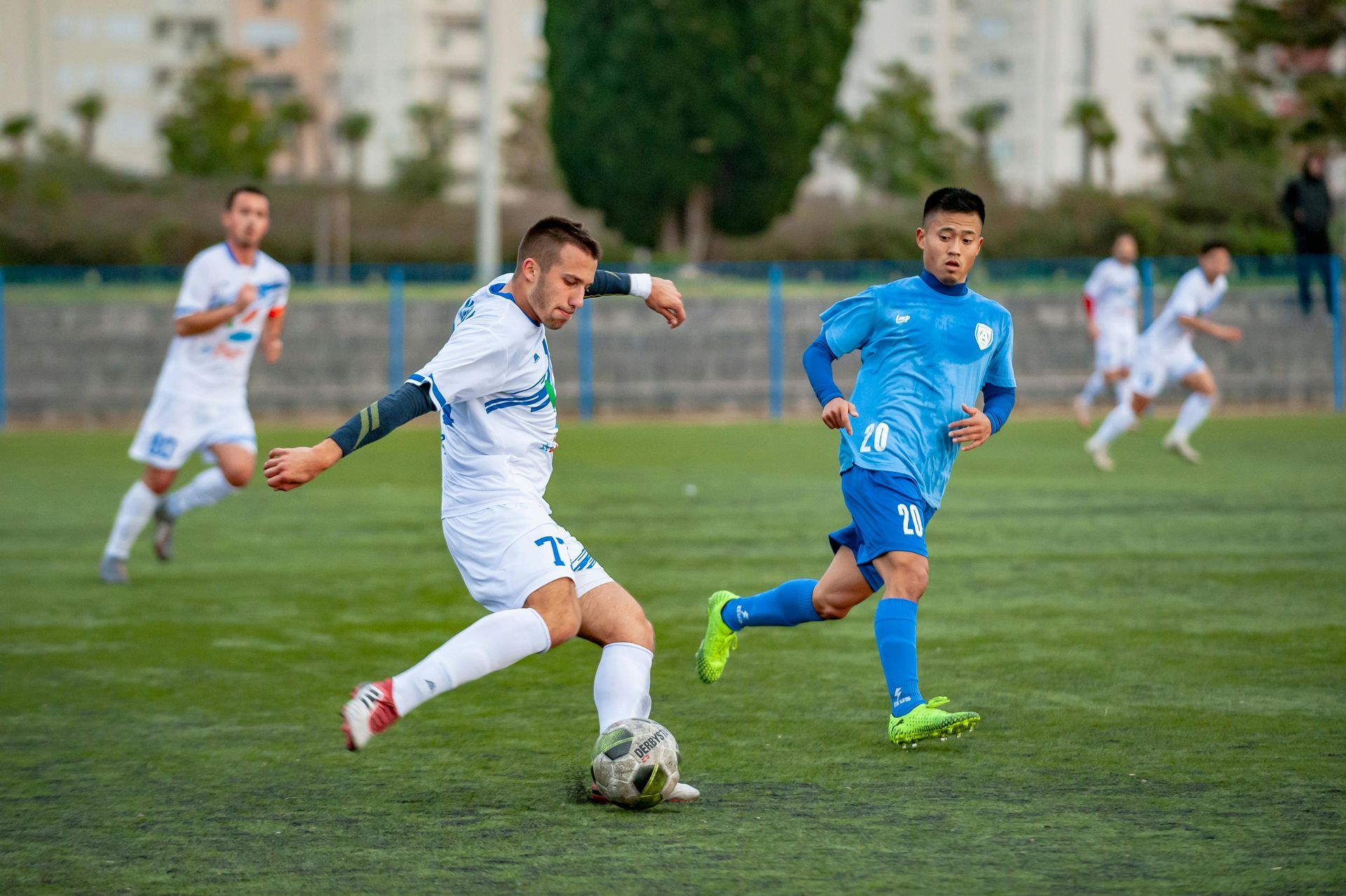Voetballers in blauw-witte tenues strijden om de bal op een grasveld.