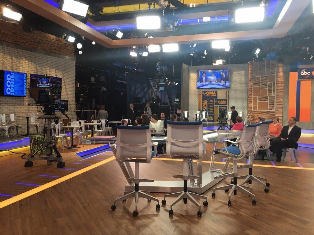 A group of people are sitting at tables in a television studio.