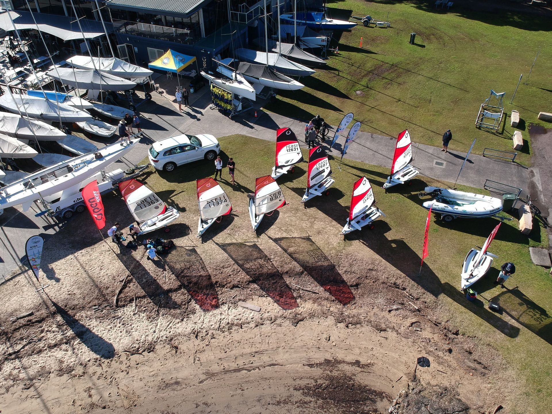 Boats on shore near a boathouse. Several windsurfers with red and white sails. — Gosford Sailing Club in Gosford, NSW