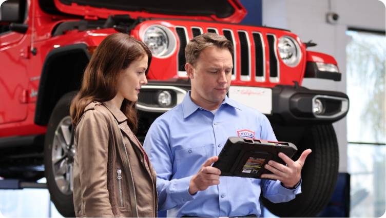 A man and a woman are looking at a tablet in front of a red jeep