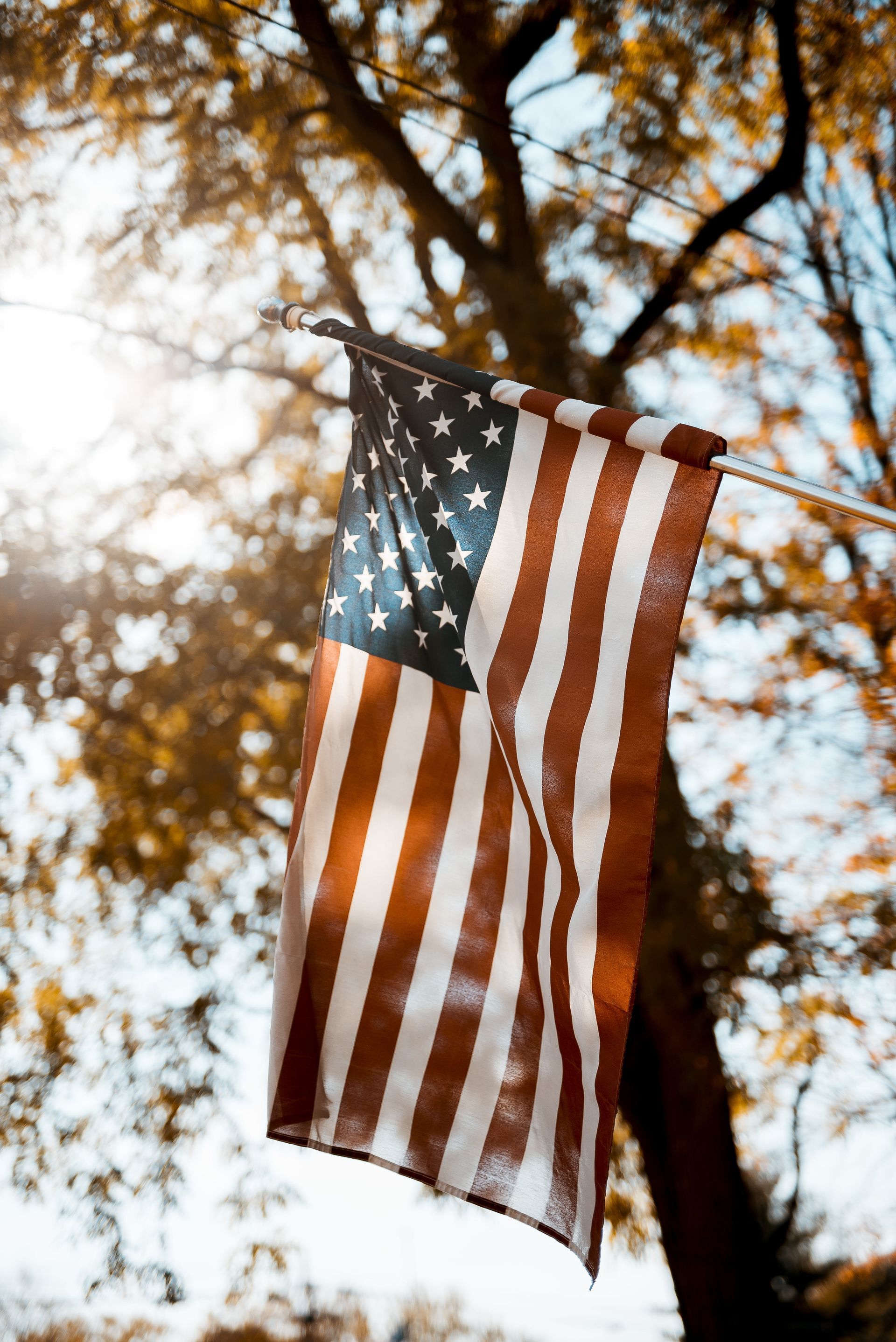 American flag hanging outside, sunlit with fall foliage in the background.