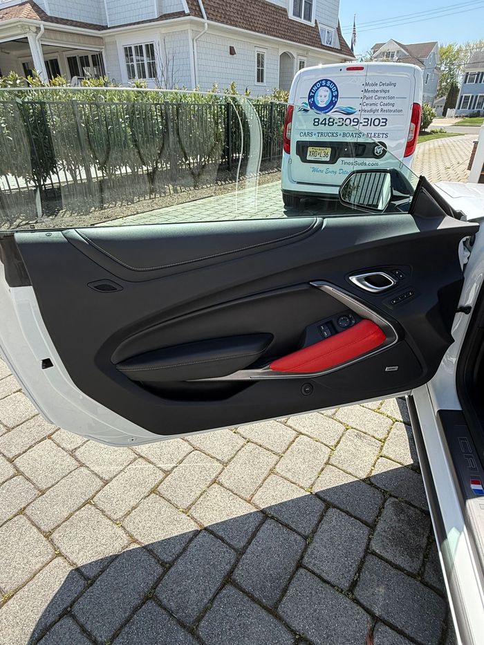 Car door interior with black trim and red accent, open beside a paved driveway and house fence