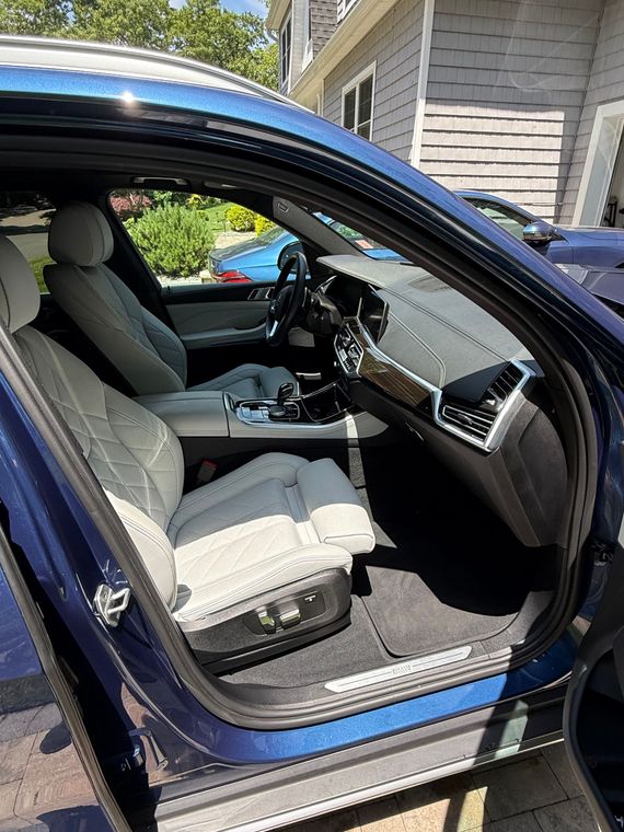 Blue car with driver door open, showing gray seats and dashboard inside a driveway.