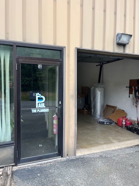 Exterior of a plumbing business with glass door and open garage. Sign on door says