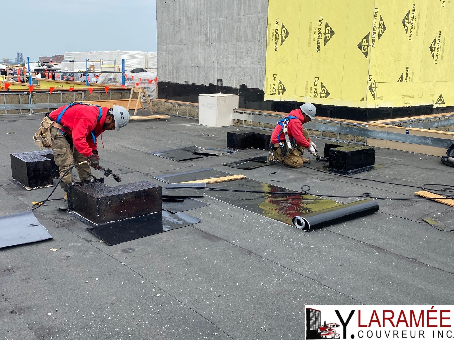 Deux hommes travaillent sur un toit avec un panneau indiquant ylaramee