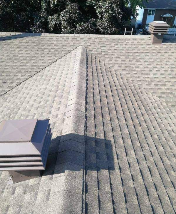 Roof with gray shingles, vents, and a central ridge, outdoors on a sunny day.