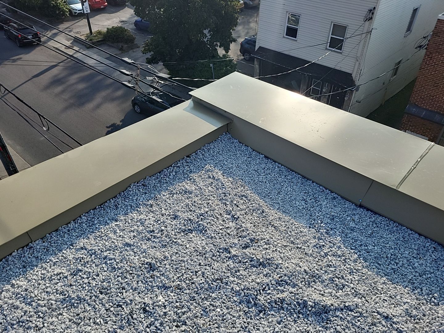 Toit plat recouvert de gravier, bordé d'une garniture métallique ; paysage urbain en arrière-plan.