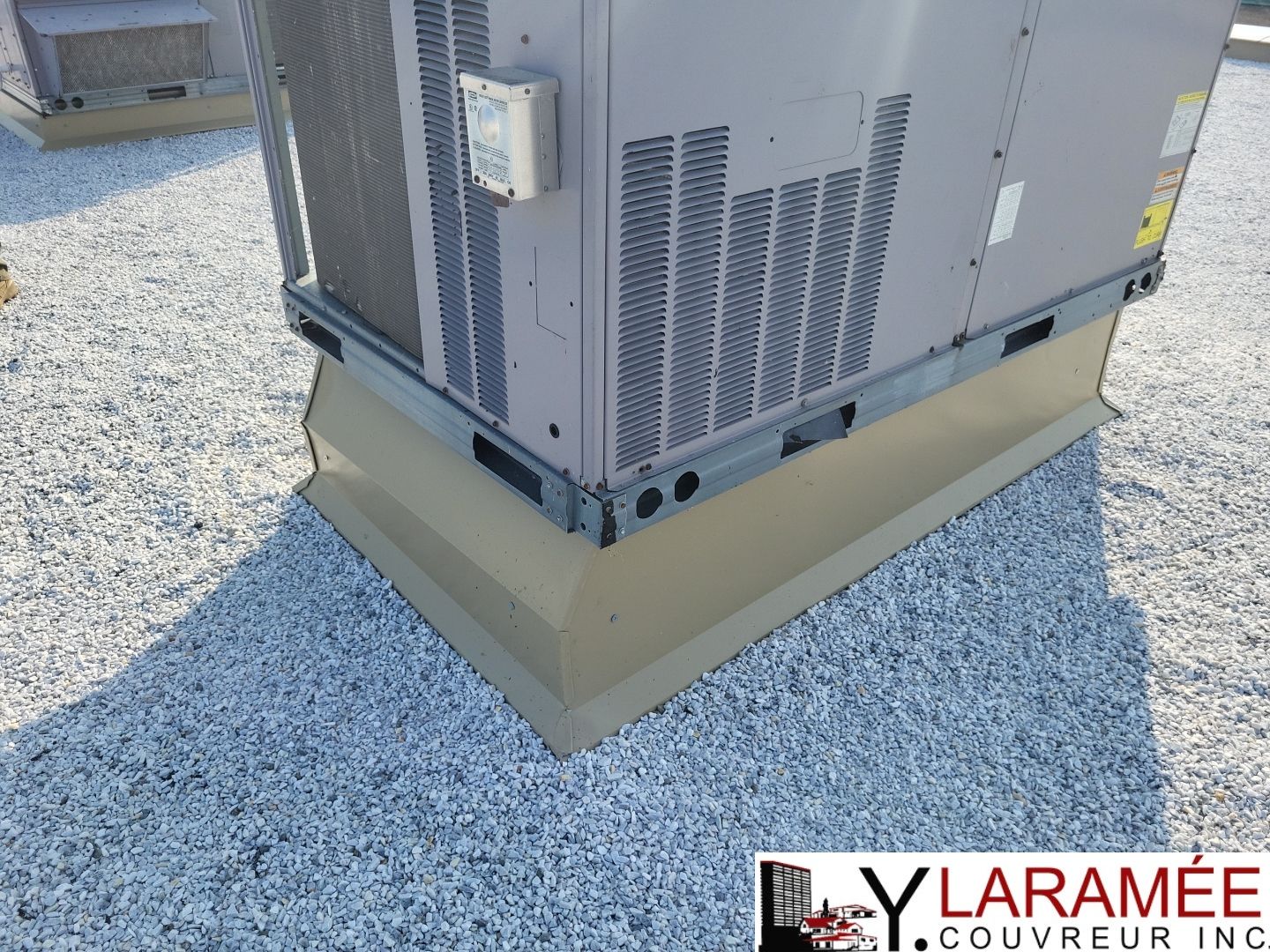 Unité de climatisation sur un toit recouvert de gravier. Unité grise sur socle beige.