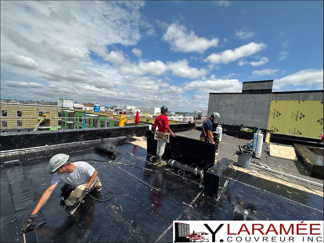 Couvreurs installant un nouveau toit plat sur un bâtiment sous un ciel bleu nuageux.