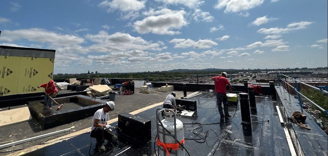 Des ouvriers installent une toiture sur un toit plat sous un ciel bleu avec des nuages épars.