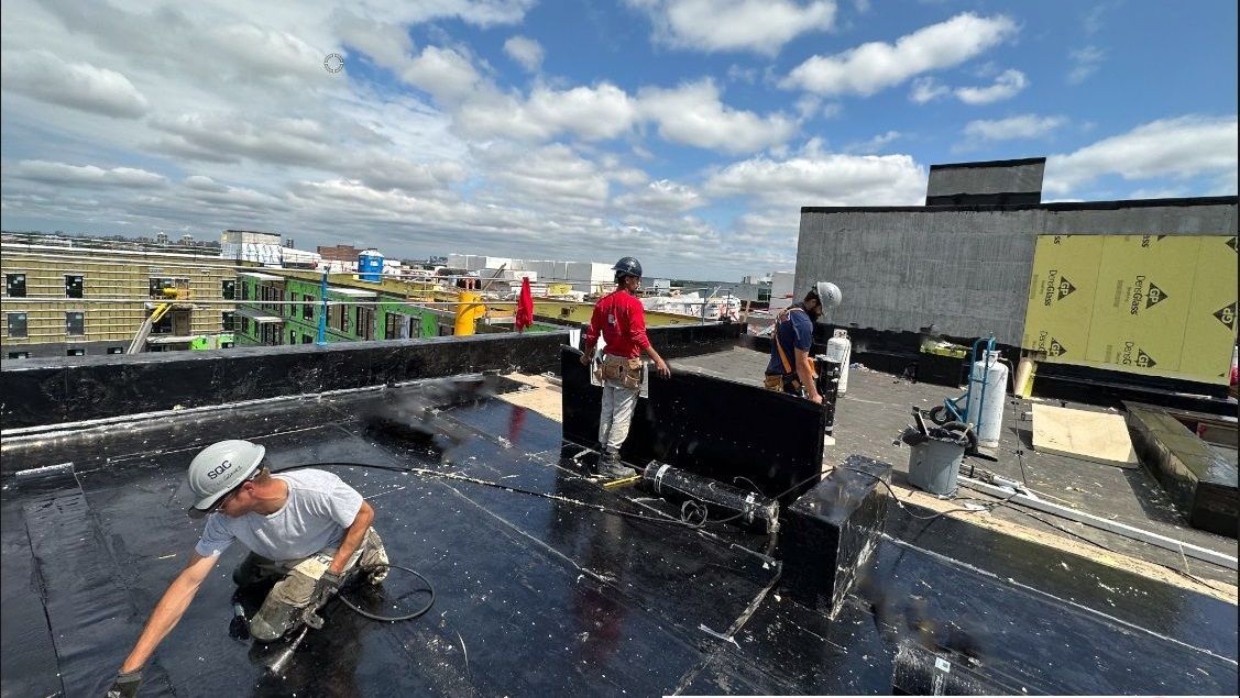 Des ouvriers du bâtiment sur un toit installent des matériaux de toiture par une journée ensoleillée.