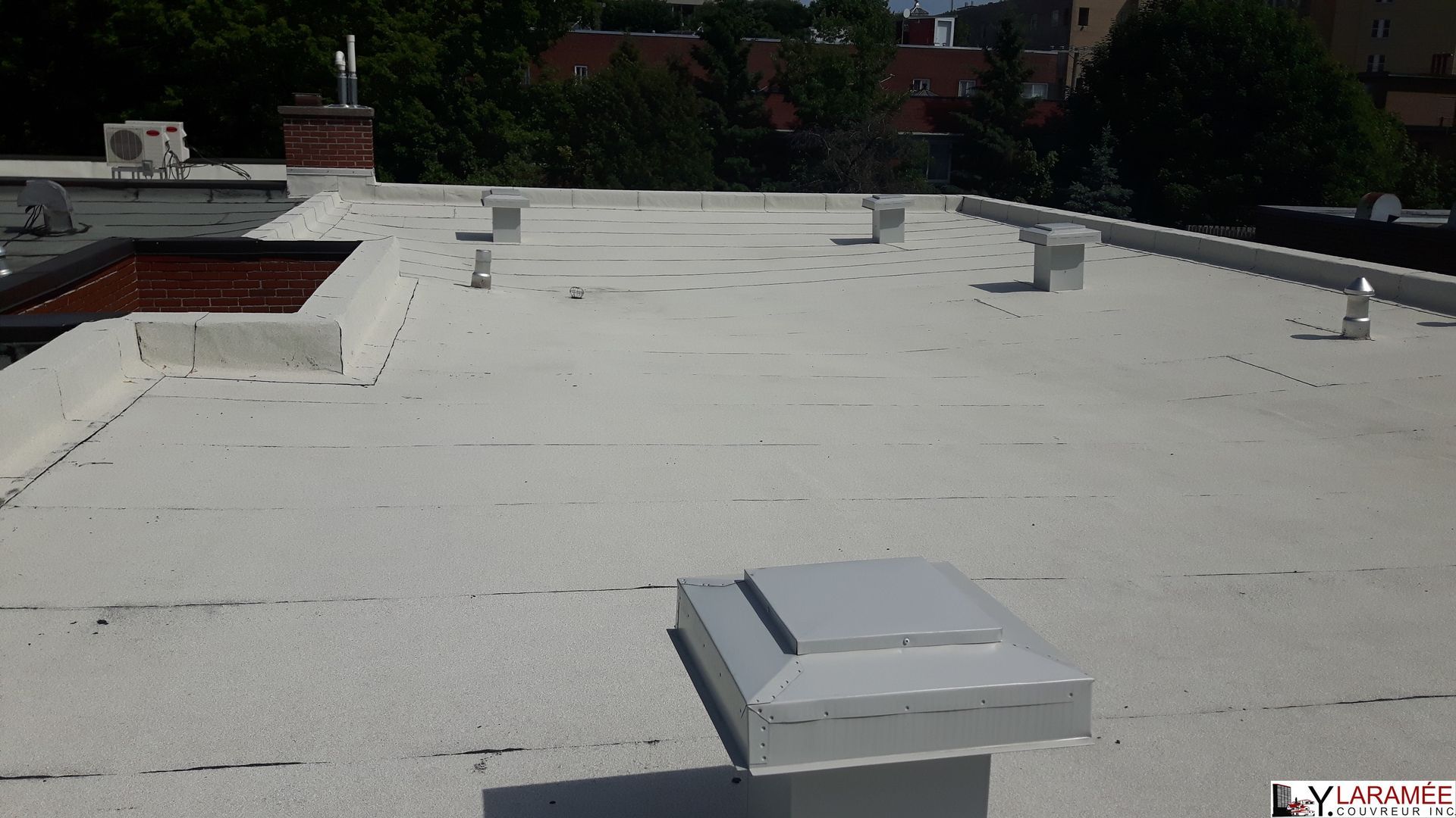 Un toit plat et blanc avec plusieurs évents rectangulaires et des bâtiments visibles en arrière-plan.