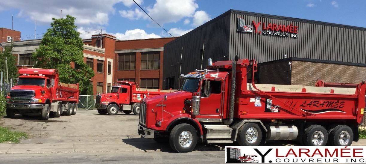 Trois camions à benne rouges sont garés devant un bâtiment.