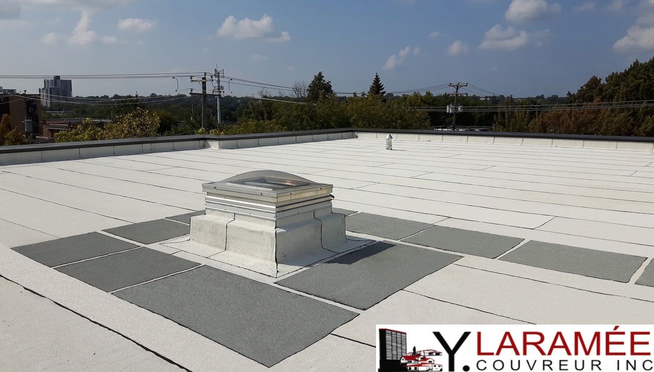 Toit plat blanc avec puits de lumière et carrés d'accent gris, cadre extérieur ensoleillé.